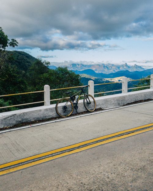 Free A bicycle rests on a mountain road with panoramic views of blue mountains and lush greenery. Stock Photo
