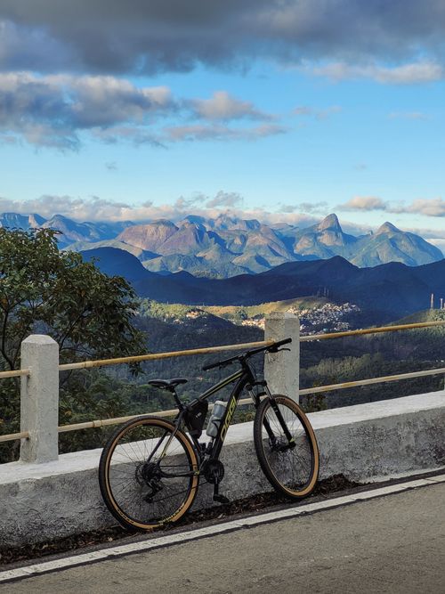 Free A mountain bike resting against a barrier on a road with breathtaking mountain scenery under a clear sky. Stock Photo