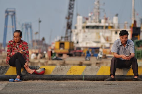 Woman and Man Sitting on Wall in Harbor