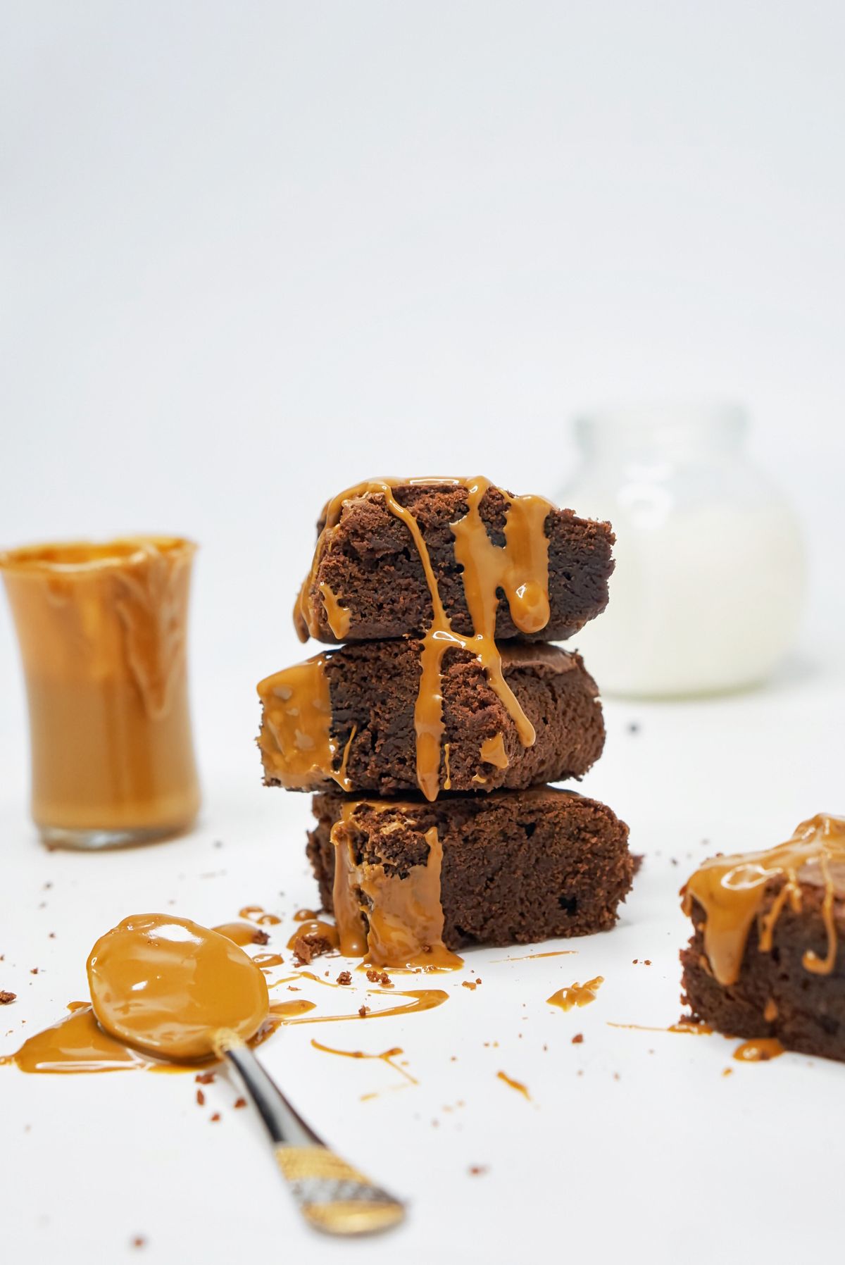 Three stacked brownies dripping with dulce de leche beside a glass of caramel and milk