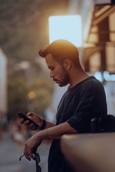 A man with beard and mustache texting on smartphone while standing outside at sunset.
