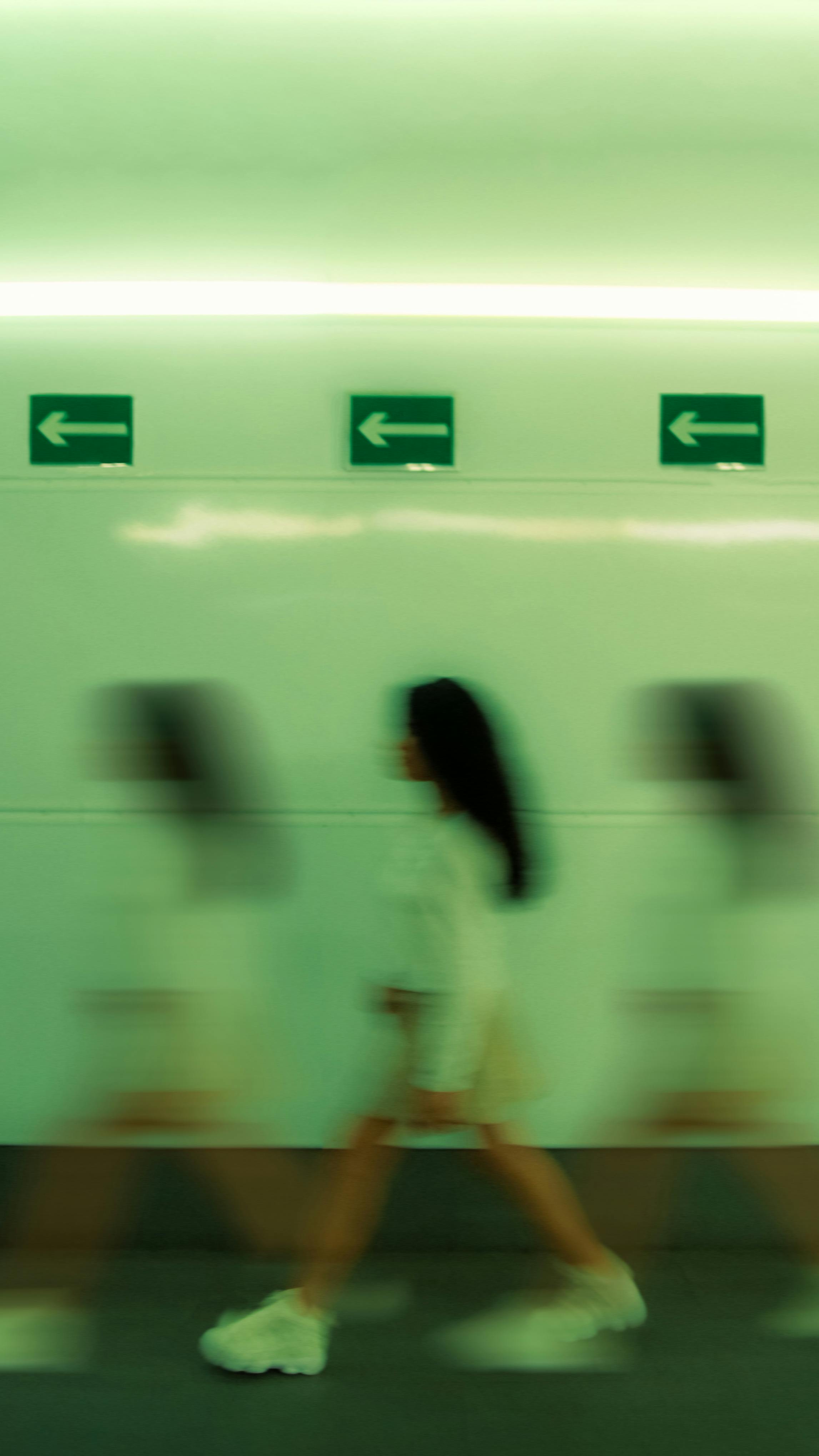 Blurred motion capture of a woman walking in a tunnel in Madrid, featuring arrow signs.
