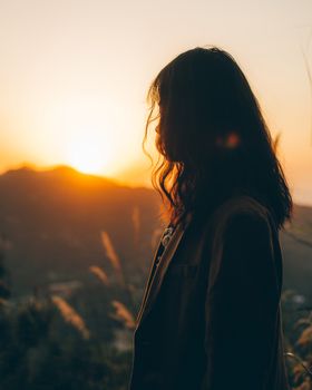 Moody silhouette of a woman standing at sunrise against a mountain landscape. Captures serene and contemplative mood.