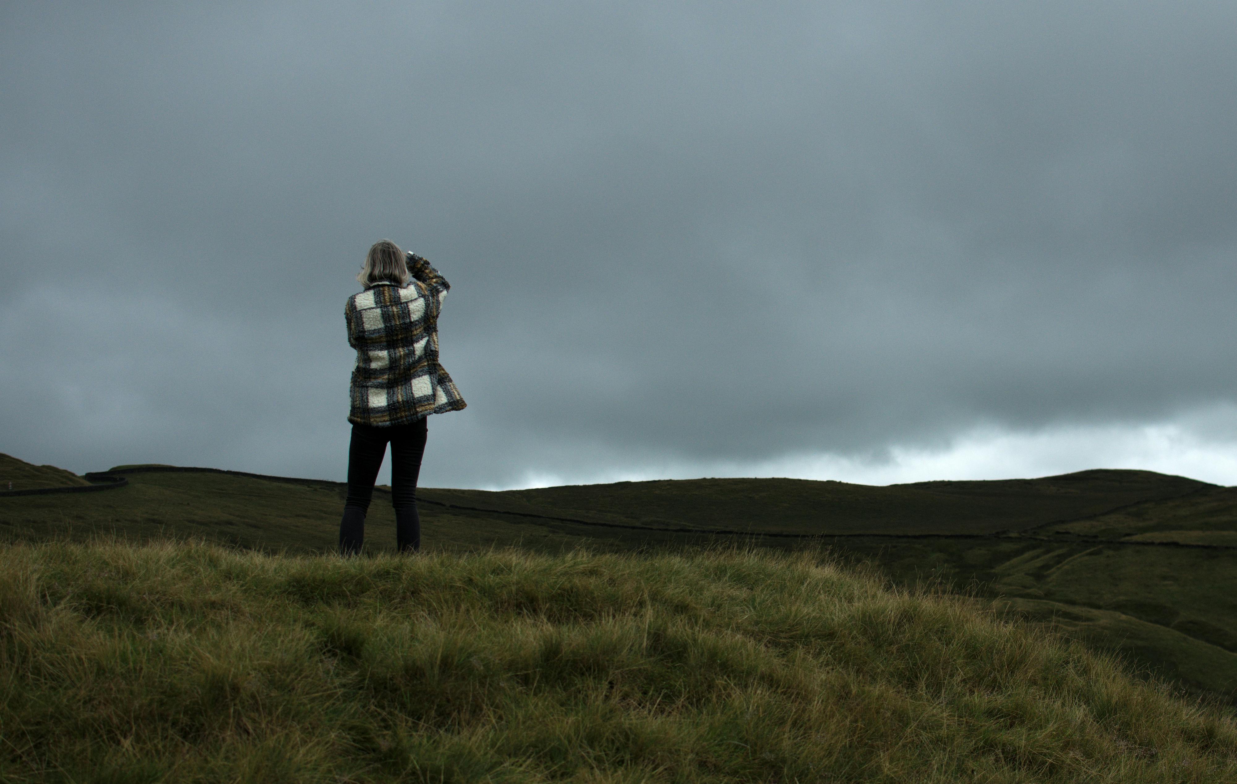 A person photographing lush green hills in Burnley, UK, under an overcast sky.