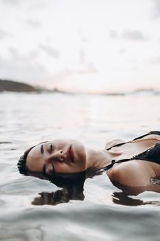 A woman in a bikini floating peacefully in the sea at sunset, evoking calm and relaxation.