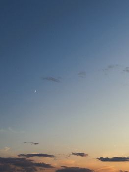 A calming view of the sky at dusk with soft clouds and a crescent moon in the background.
