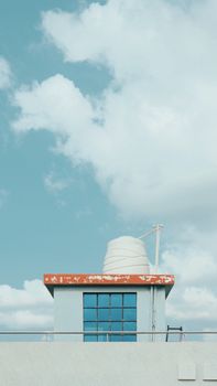 A minimalist rooftop with water tank against a blue sky with fluffy clouds, emphasizing architecture.