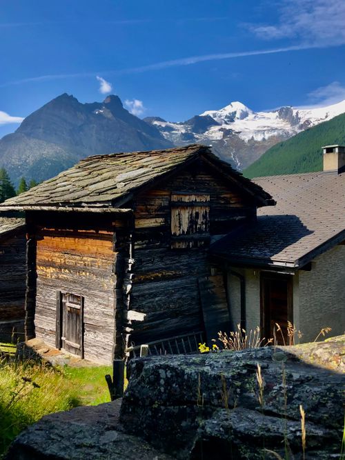 Free Picturesque view of a rustic wooden house in an alpine village with stunning mountain backdrop. Stock Photo