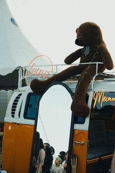 A giant teddy bear sits atop a vintage food truck at an outdoor festival market.