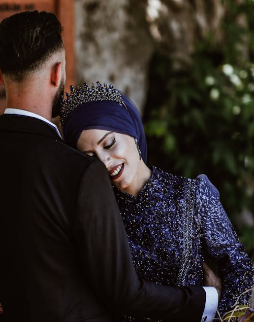 Man in Black Suit Embracing his Bride in Blue Wedding Dress and Headscarf