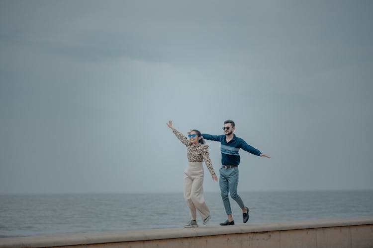 Young Couple Balancing On A Waterfront Wall