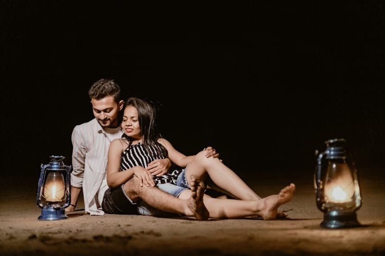 Young Couple Lying On A Sand Beach With Retro Lanterns