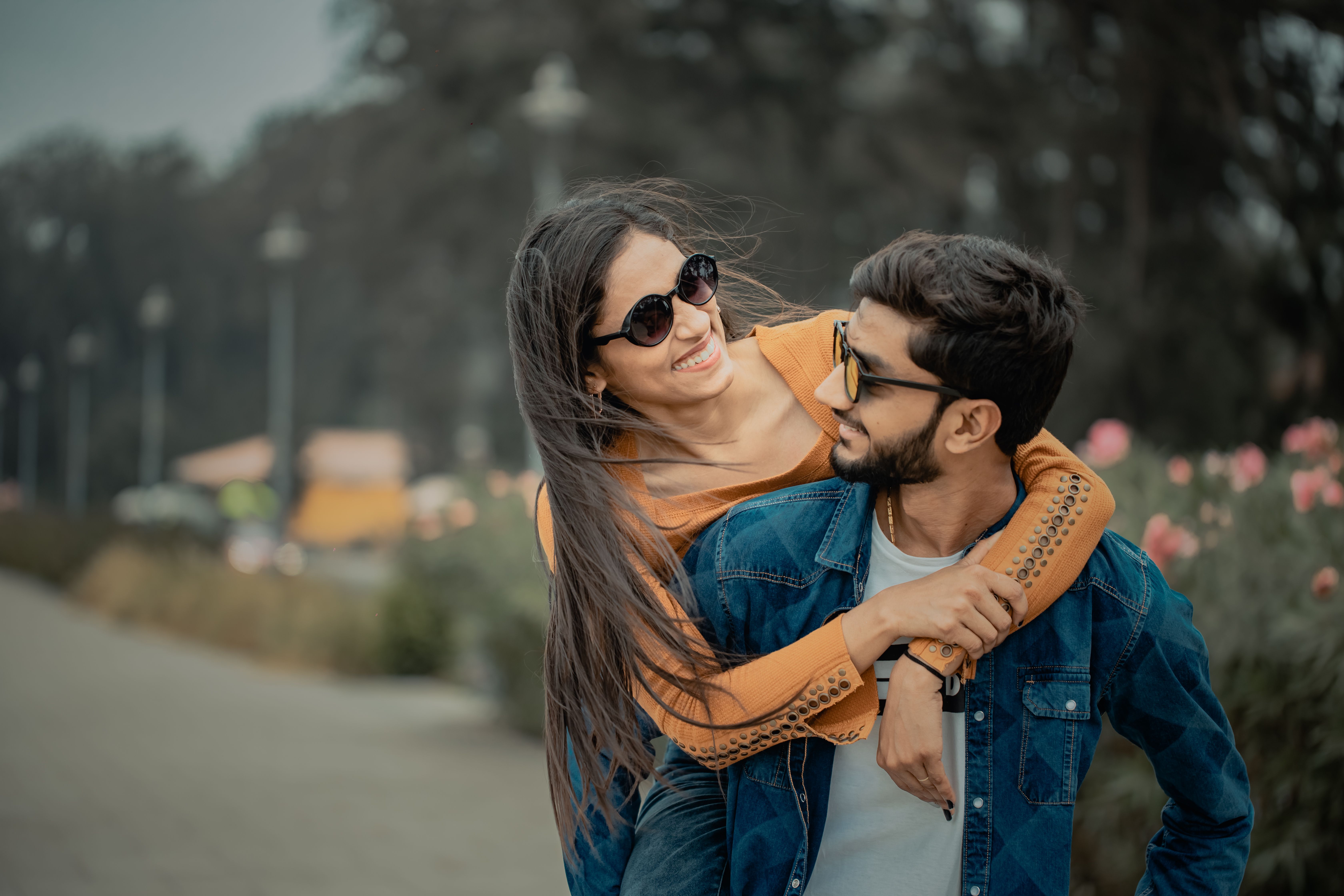 A happy couple wearing sunglasses embracing outdoors, showcasing love and leisure in a scenic setting.