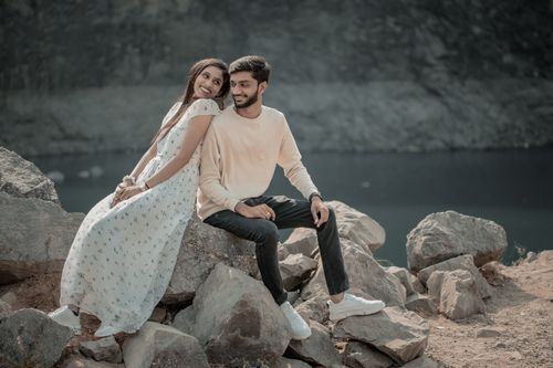 Free A couple enjoying a romantic moment sitting on rocks by a serene lake. Stock Photo