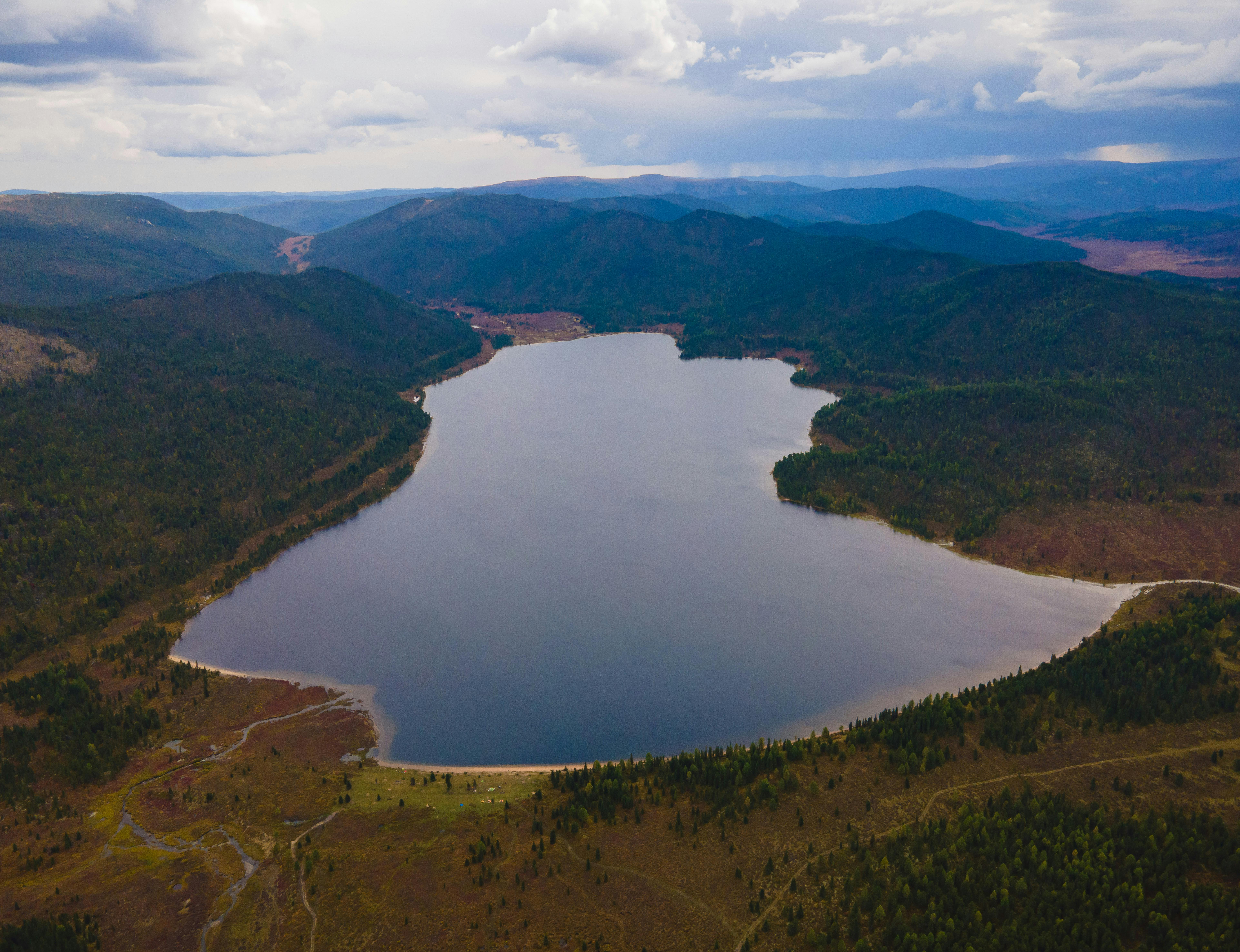 Stunning aerial view of a tranquil lake surrounded by lush hills and dramatic skies.