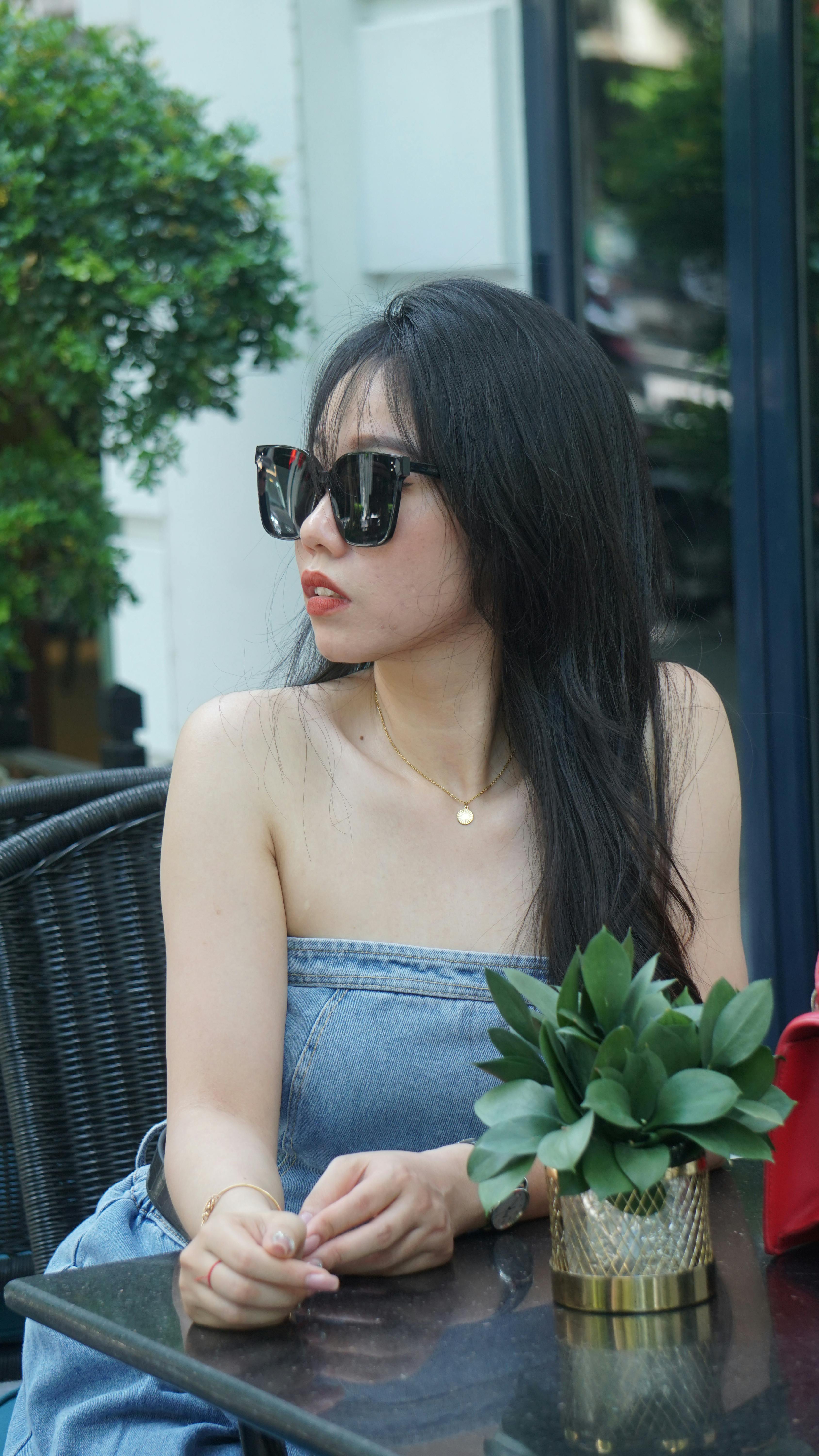 Stylish Asian woman with sunglasses sitting outdoors in a modern urban cafe setting.