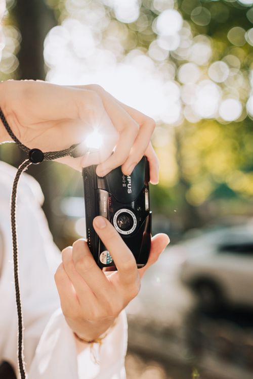 Free Hands holding a vintage film camera with sunlight creating a lens flare outdoors. Stock Photo
