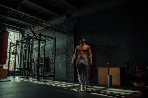 Free A muscular man poses confidently in a dimly lit gym, highlighting his toned physique. Stock Photo