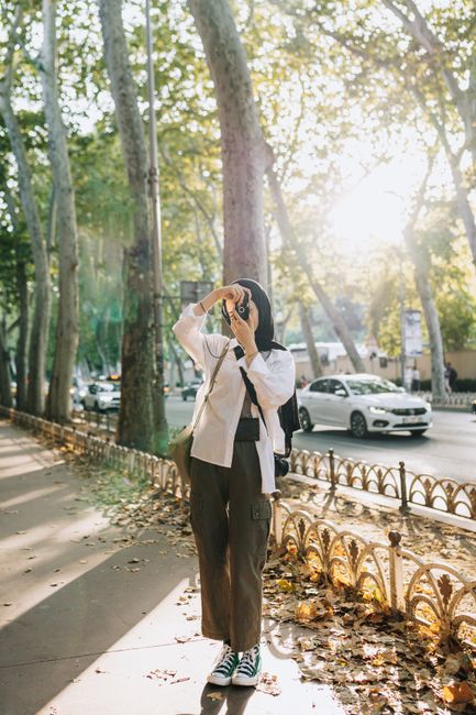 A woman in casual attire takes photos on a sunlit sidewalk in Istanbul, Turkey.