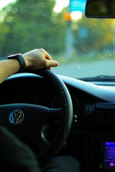 Close-up of a man driving a Volkswagen car, holding the steering wheel with one hand wearing a wristwatch.