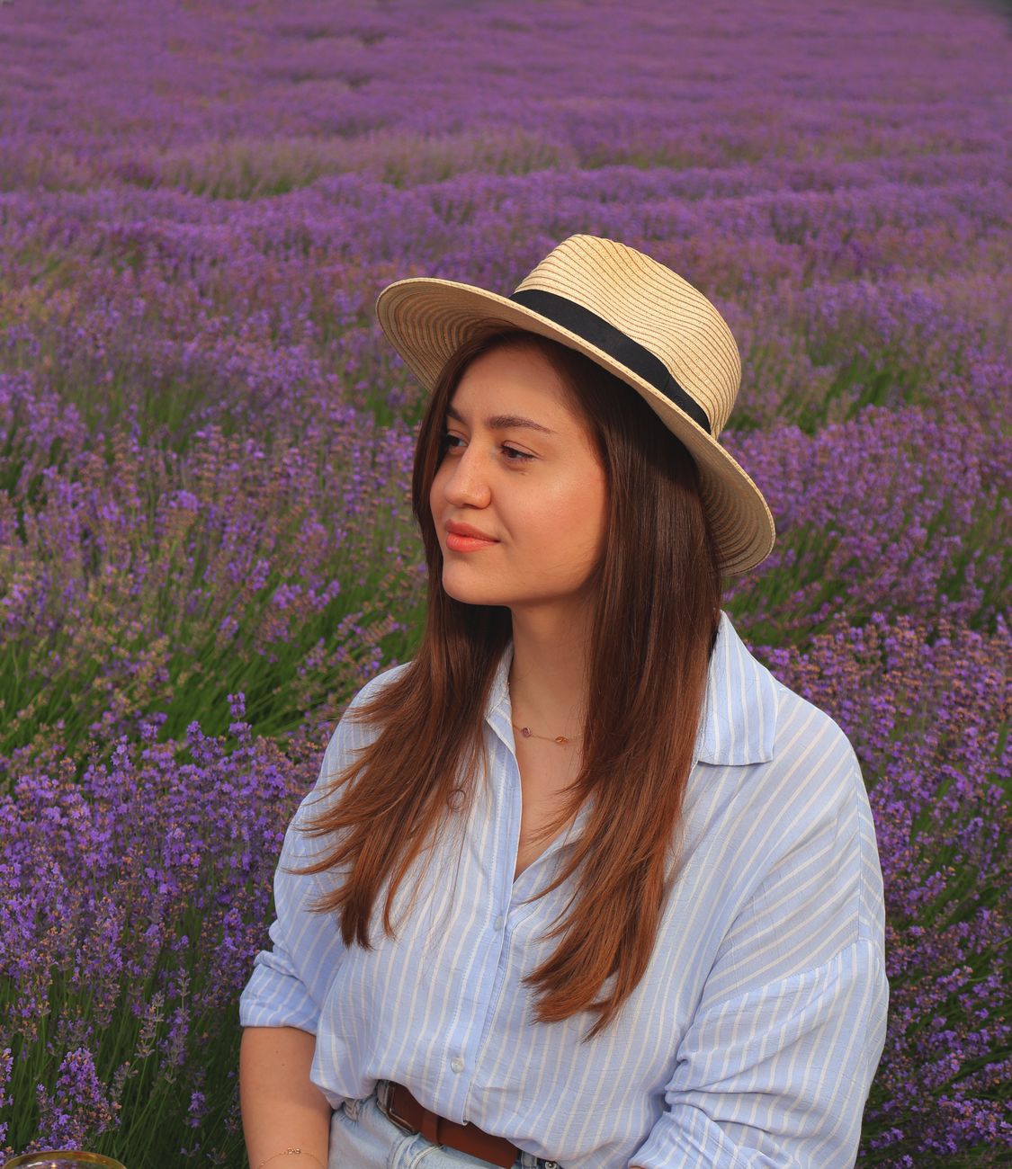 Woman with straw hat enjoying a peaceful moment in a blooming lavender field.