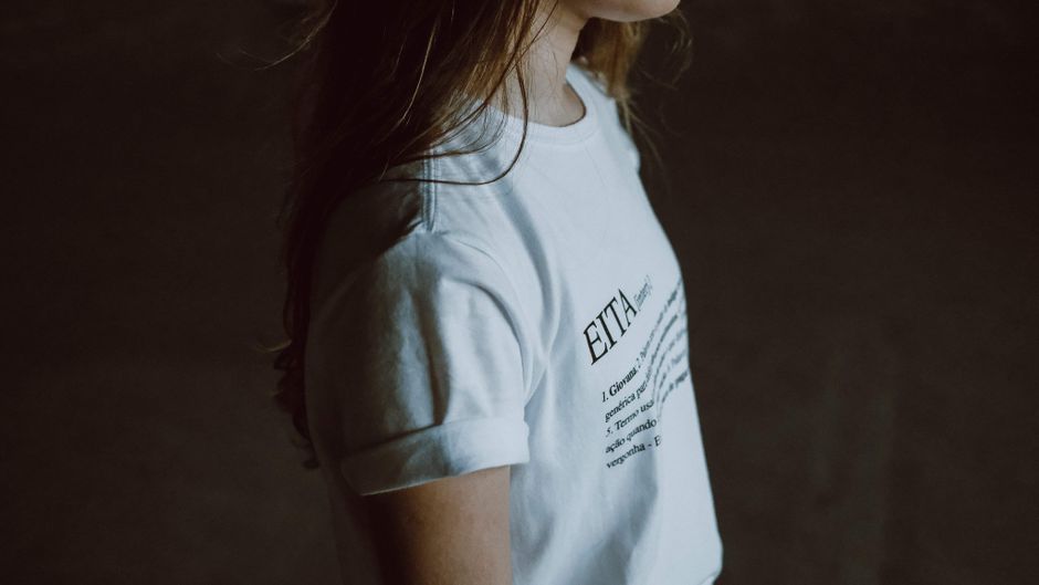 Side profile of a woman wearing a white t-shirt with printed text on a dark background.
