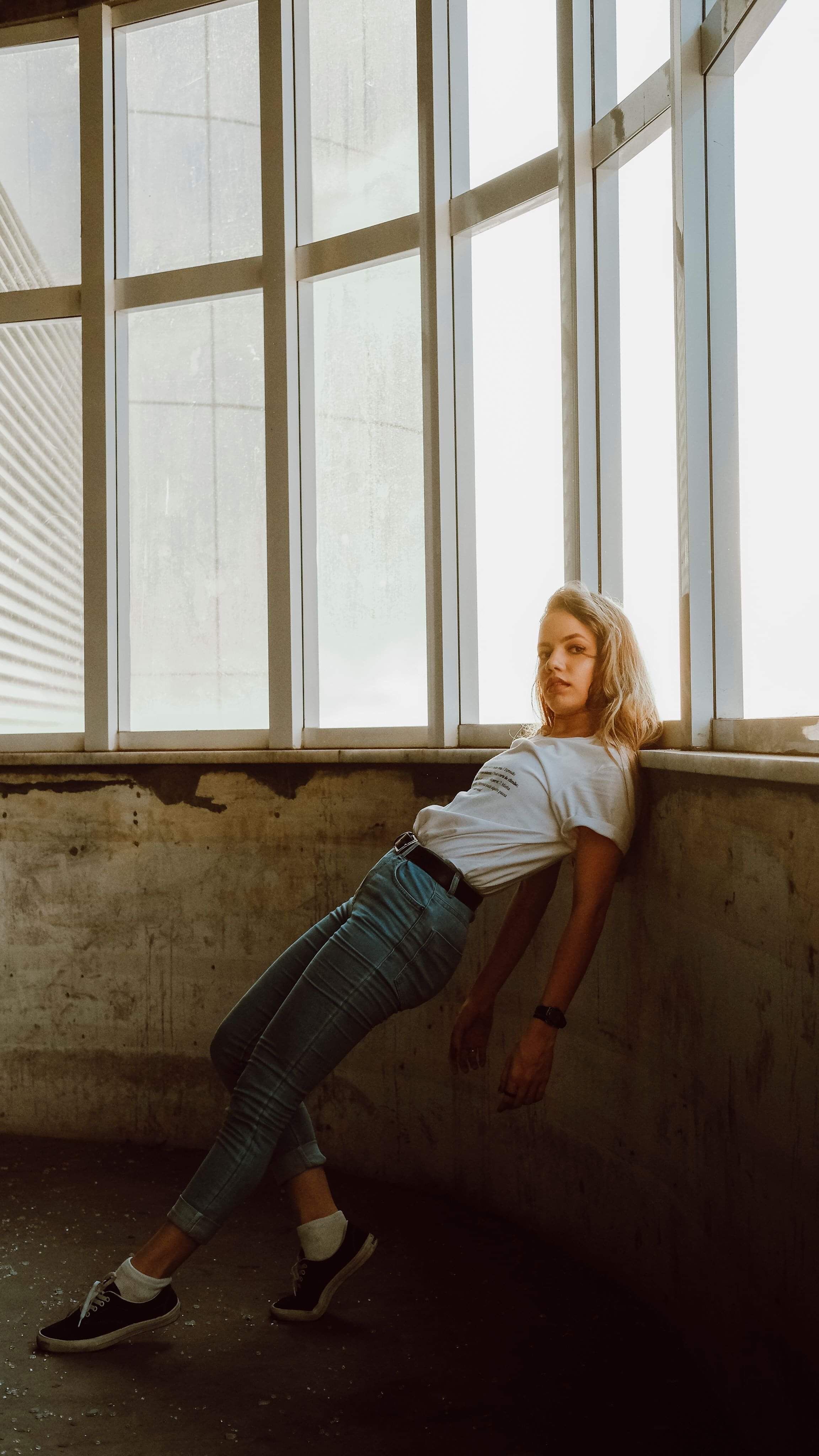 Stylish woman posing by window in urban setting. Trendy fashion and dramatic lighting.