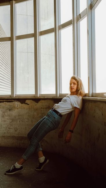 Stylish woman posing by window in urban setting. Trendy fashion and dramatic lighting.