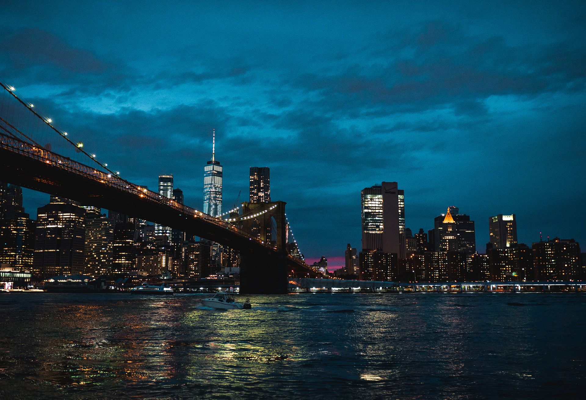 Stunning night view of New York City skyline featuring illuminated Brooklyn Bridge over the river.