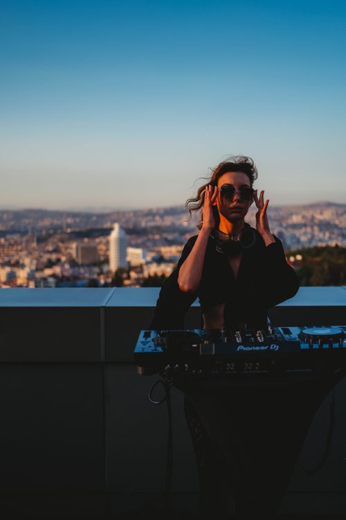 Free A DJ with sunglasses mixing music on a rooftop overlooking Ankara at sunset. Stock Photo