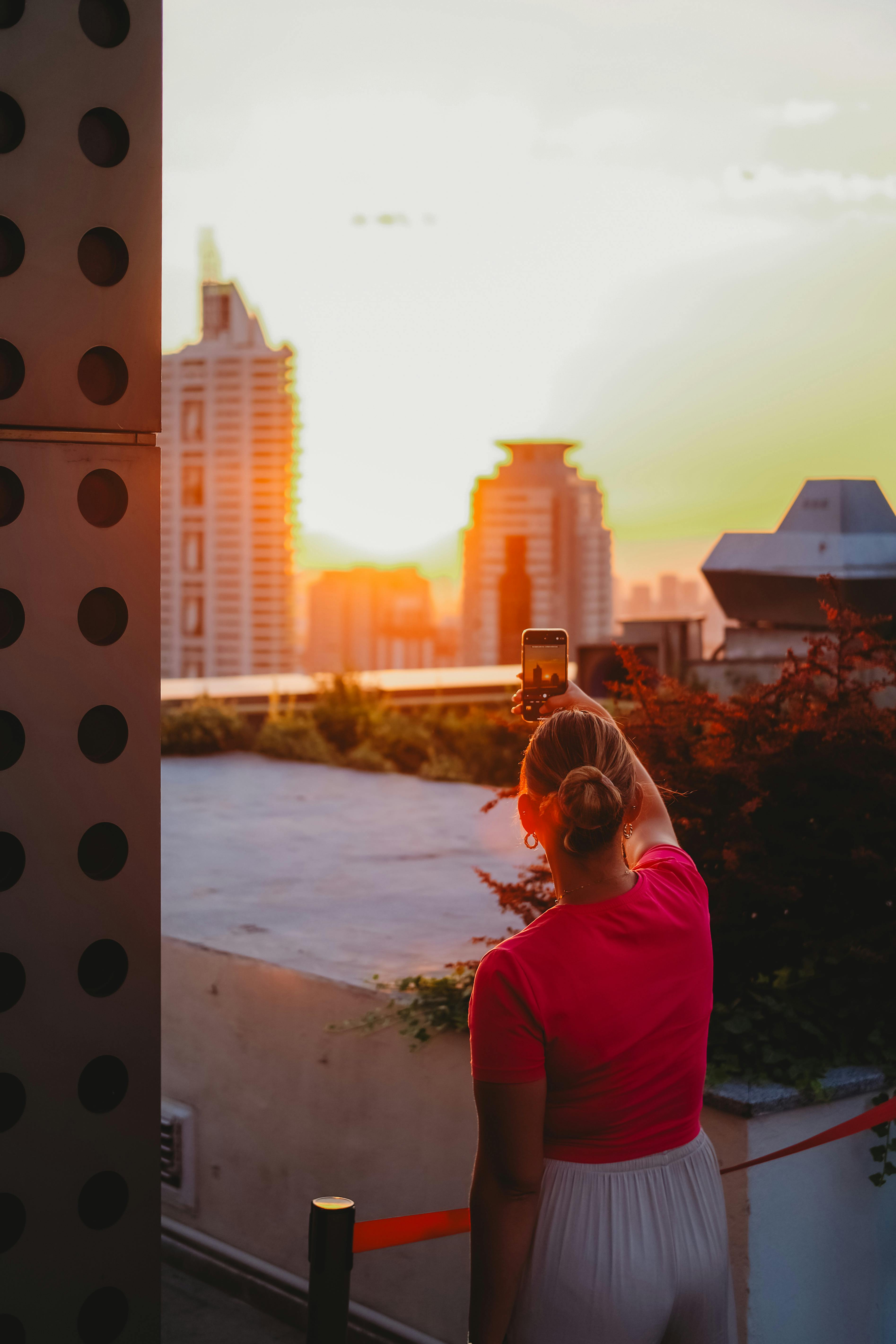Free A woman photographs the Ankara skyline during a vibrant sunset with her smartphone. Stock Photo