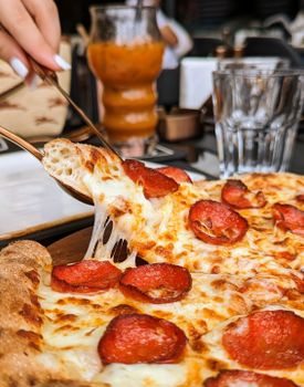 Close-up of a mouthwatering pepperoni pizza slice with melted cheese being served in a restaurant setting.