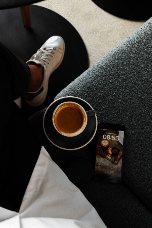 Free A cozy scene of relaxing with coffee, smartphone, and casual sneakers on a sofa. Stock Photo