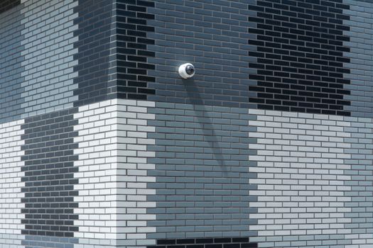 Grayscale facade featuring geometric brick pattern and surveillance camera, modern architecture.