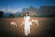 Woman in White Dress among Sheep on Pasture
