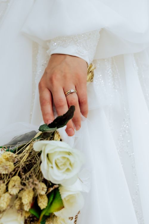 Free Close-up of a bride's hand holding a bouquet, featuring a beautiful wedding ring. Stock Photo