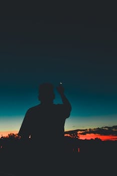 黄昏时分，一个男人指着夜空中的剪影，背景是充满活力的日落色彩