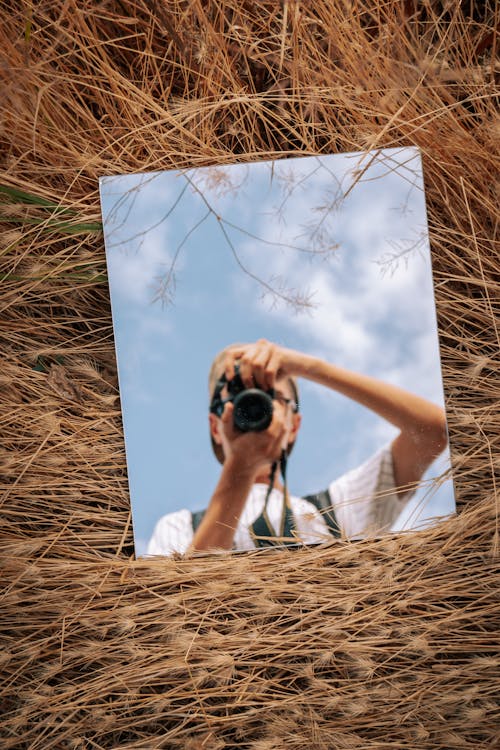 Man Using a Camera Reflecting in a Mirror Lying on the Grass