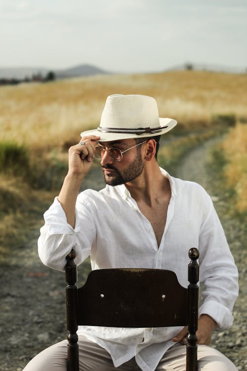 Portrait of a Male Model Wearing a Fedora Sitting in the Middle of a Rural Dirt Road