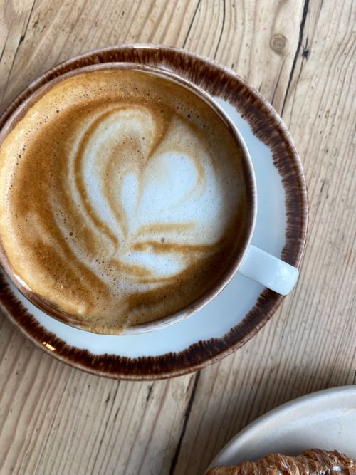 Free Delightful latte art in a coffee cup, paired with a croissant, shot from above. Stock Photo