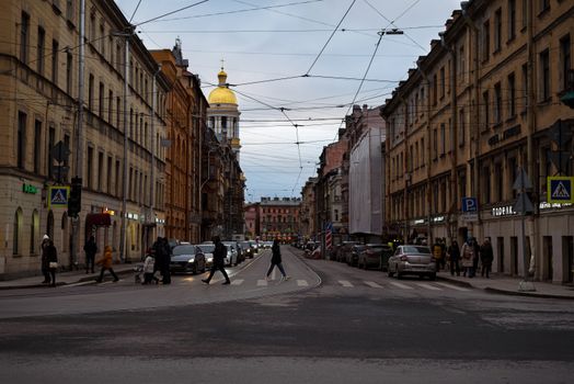 A vibrant city street with pedestrians crossing and classic buildings lining the road.