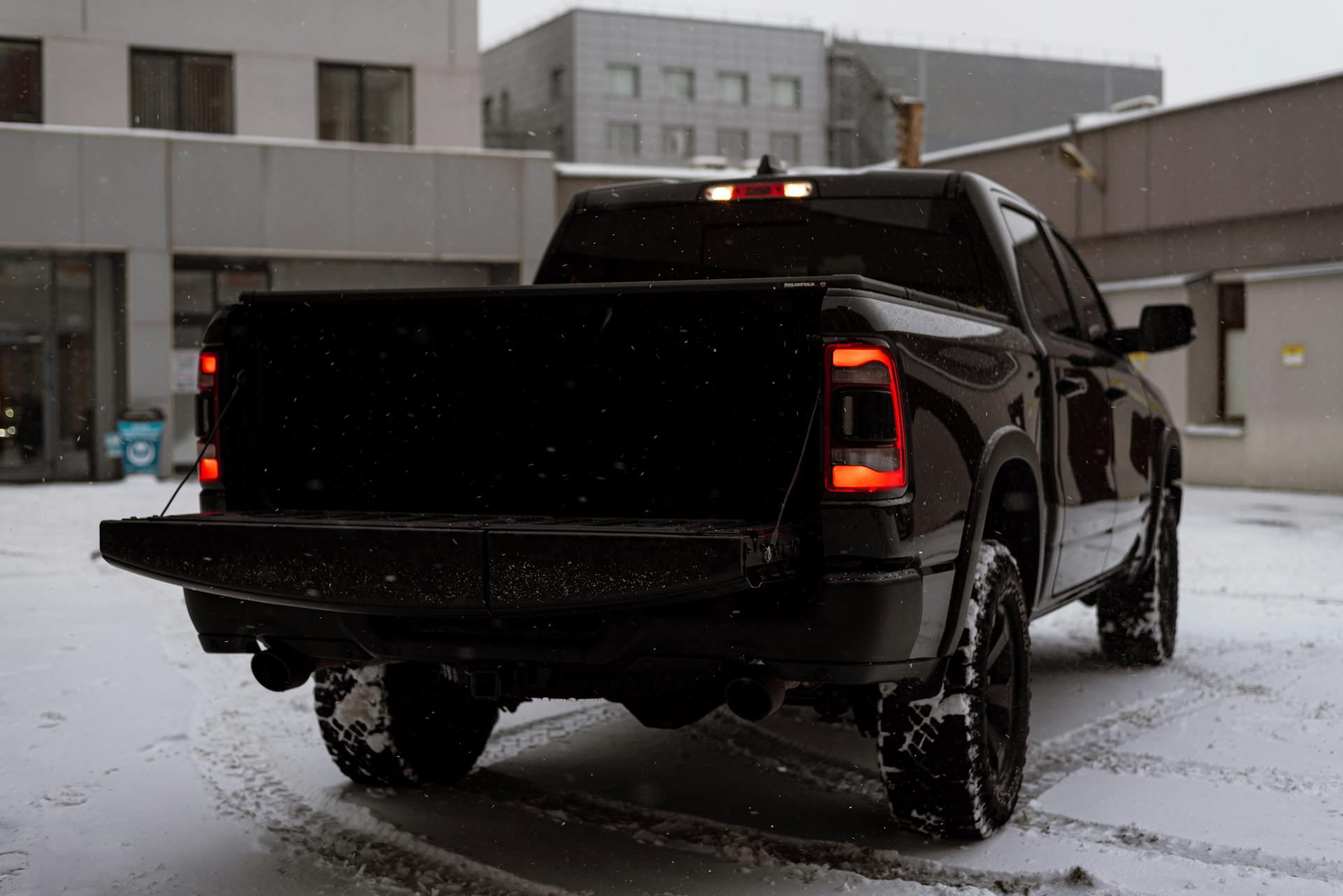 Black pickup truck parked on snow-covered urban street with falling snowflakes.