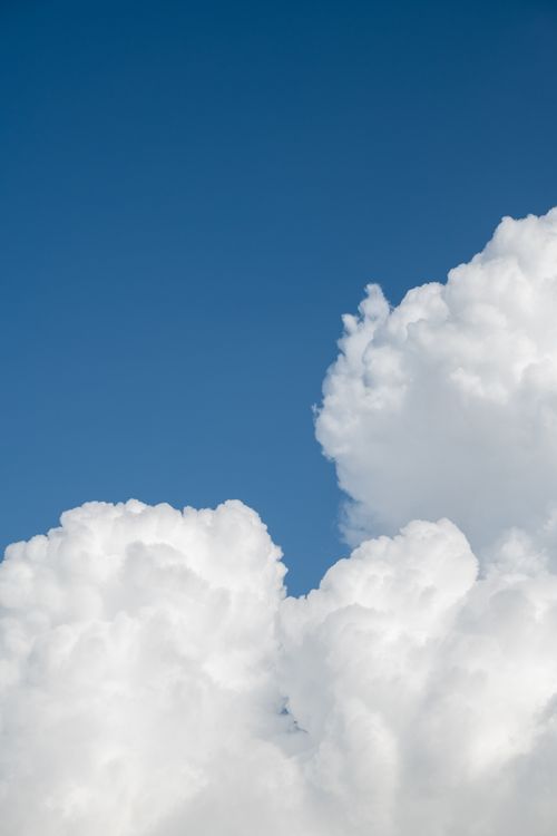 Free A vivid view of fluffy cumulus clouds on a sunny day against a clear blue sky. Stock Photo