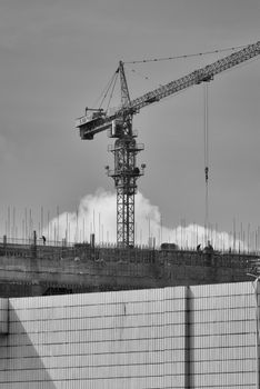 Black and white image of a tower crane at an urban construction site with workers.