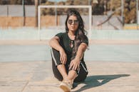 一位戴着太阳镜、身着休闲装的时尚女性，自信地坐在户外球场上