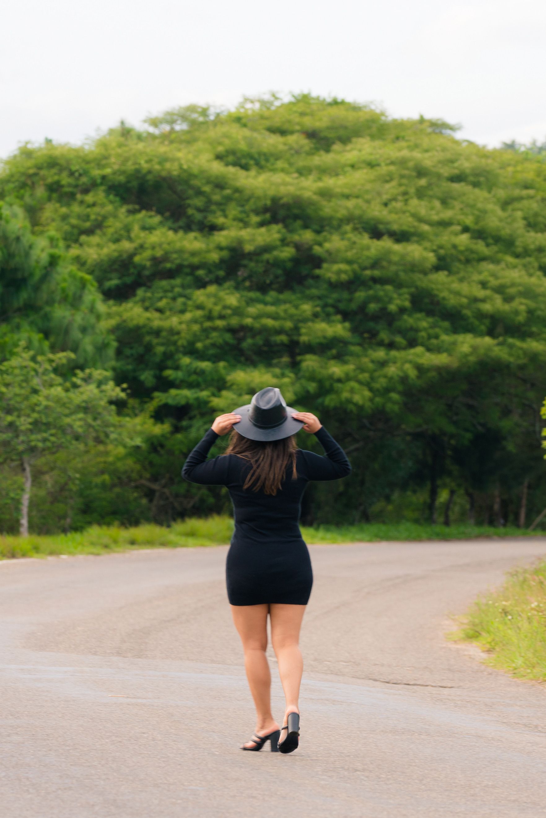 A woman in a black dress and hat walking down a road · Free Stock Photo
