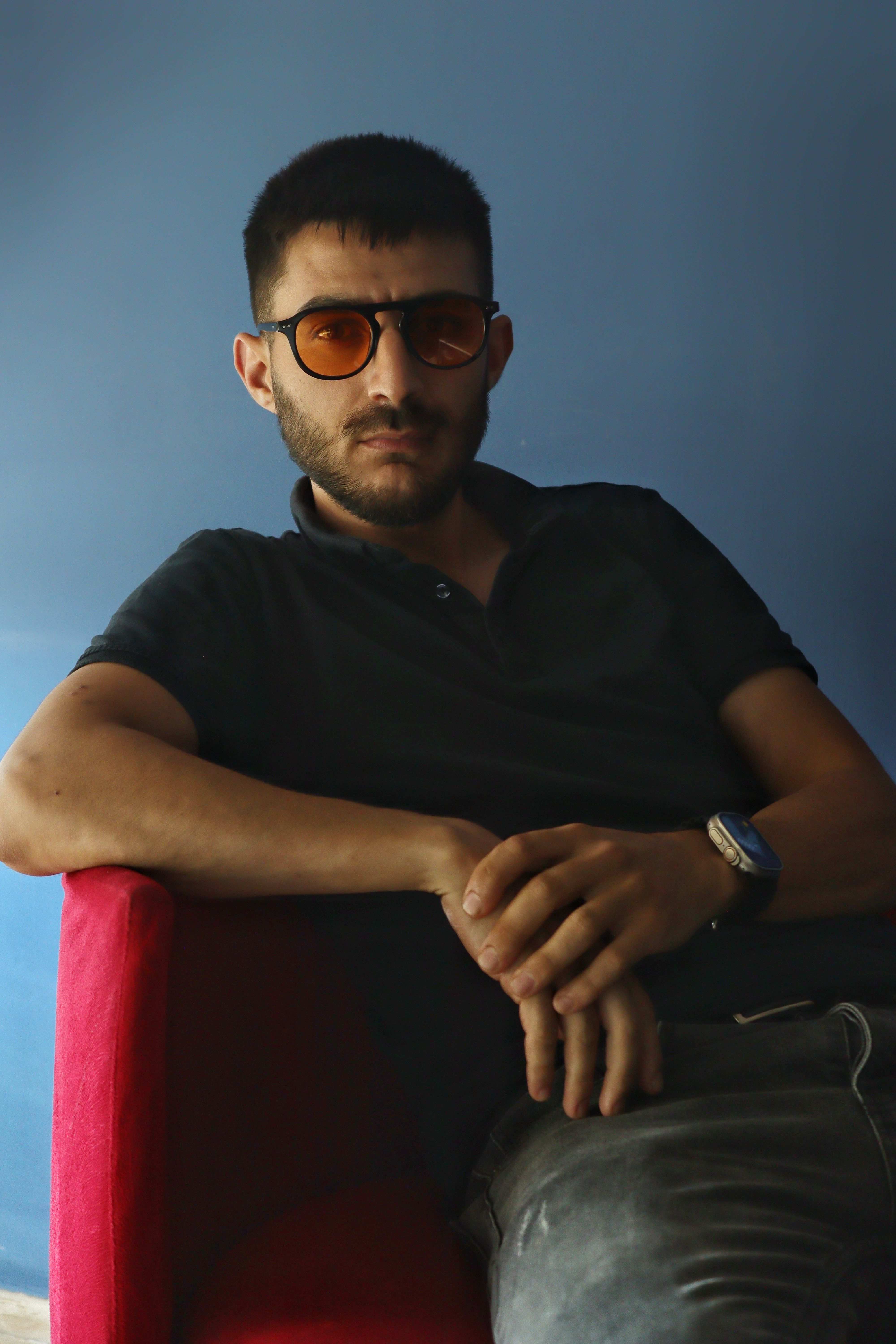 Casual portrait of a man wearing sunglasses, seated indoors on a red chair.