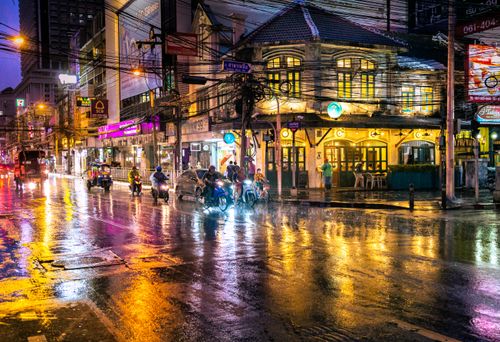 Free Explore the vibrant nightlife of Bangkok on a rainy evening, with bustling streets and neon lights reflecting in water. Stock Photo
