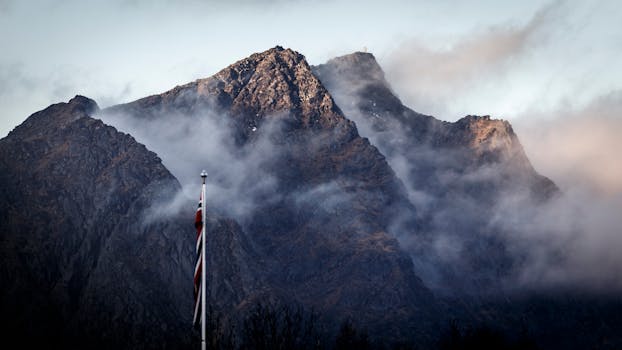 Dramatic misty mountain scene with a Norwegian flag in the foreground.