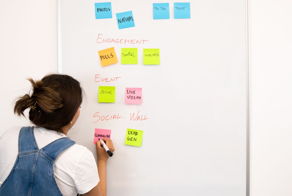 A woman organizing colorful sticky notes on an office whiteboard